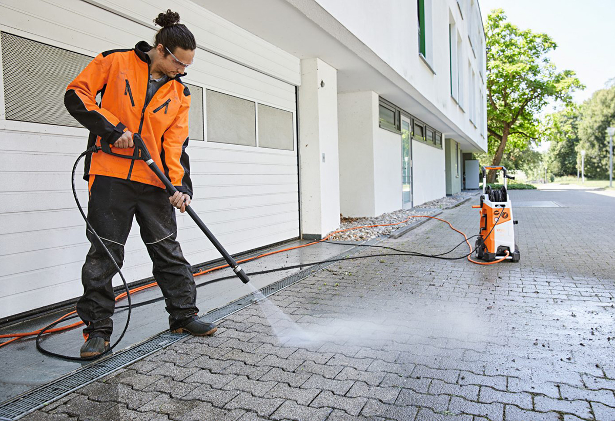 Απεικονίζεται ένας άνδρας να χρησιμοποιεί το πλυστικό RE 170 Plus για πλυνει έναν πλακόστρωτο δρόμο.